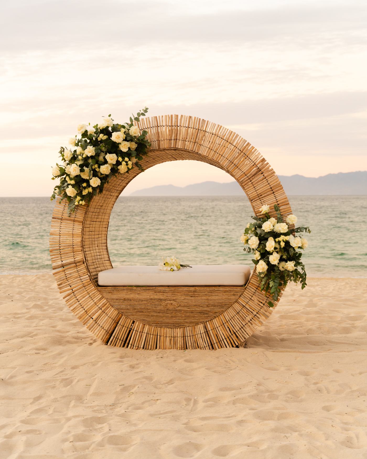 Arco circular de ratán con rosas blancas frente al mar