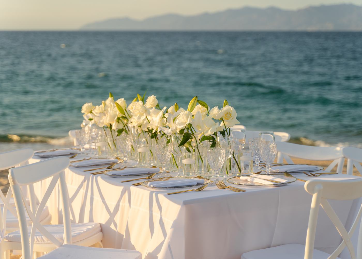 Mesa larga con sillas blancas y flores frente al Mar de Cortés